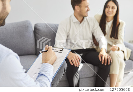 Happy smiling young couple sitting on couch at counselor's office, listening advices and smiling. Happy smiling young couple sitting on couch at counselor's office, listening advices and smiling. 127305668