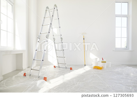 Step ladder with bucket and paint roller standing in empty light room in new house with white walls 127305693