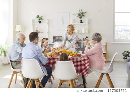 Happy mother bringing pizza at festive table for her big family during holiday celebration 127305751