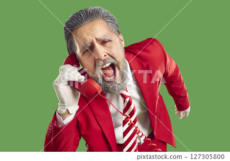 Positive, extravagant, stylish, young Santa Claus, dressed in classic stylish red suit, screams with his mouth open into the phone receiver. 127305800