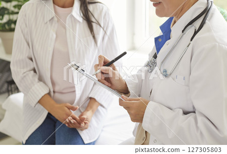 Close up female doctor holding clipboard, filling patient form, documents, medical history  127305803