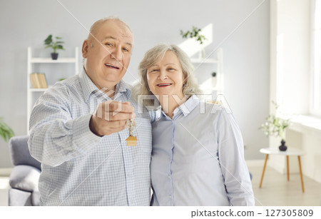 Happy senior couple holding a key in their hands standing in a new apartment on moving day. Happy senior couple holding a key in their hands standing in a new apartment on moving day. 127305809