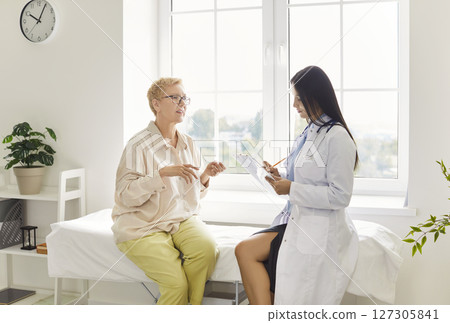Adult woman sitting on couch, discussing health concerns with doctor while physician taking notes. 127305841