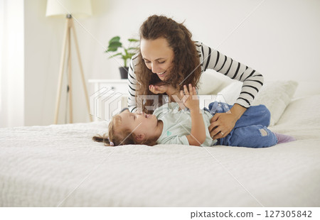 Happy, loving mother cuddling and tickling her little child daughter on the bed at home 127305842