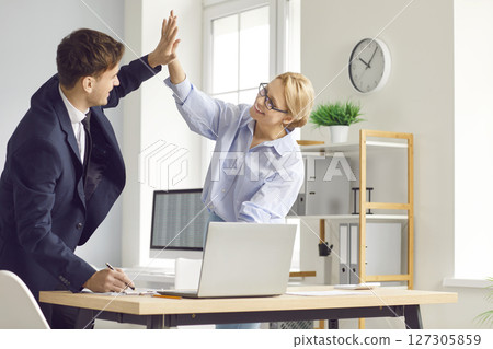 Two joyful colleagues giving high five in modern office, celebrating successful achievement at work. Two joyful colleagues giving high five in modern office, celebrating successful achievement at work. 127305859