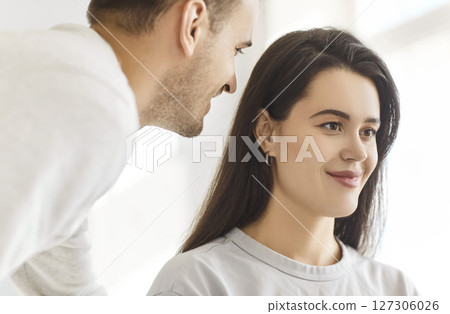 Young man whispering in the ear of brunette woman telling her secret or gossip sharing news 127306026