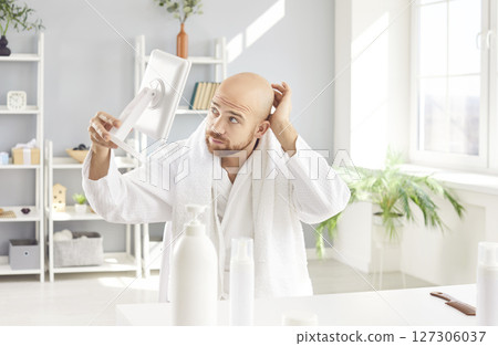 Bald Man Examining Hair Loss In Mirror 127306037