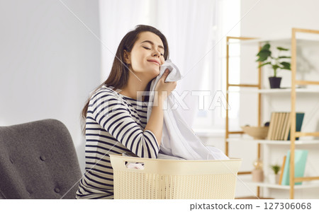 Happy woman inhales aroma of freshly washed laundry, enjoying feeling of cleanliness and freshness. 127306068
