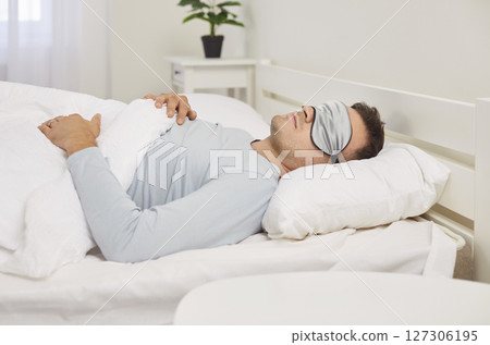 Man Sleeping In Bed At Home Early In The Morning Wearing A Sleep Mask Man Sleeping In Bed At Home Early In The Morning Wearing A Sleep Mask 127306195