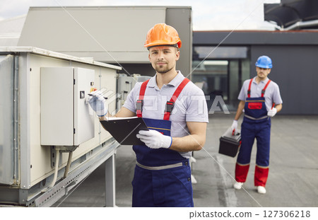 Focused Worker Inspecting HVAC System on Roof 127306218