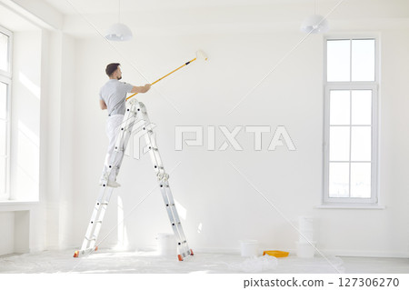 Male Painter Using Roller To Paint Wall During Home Renovation 127306270