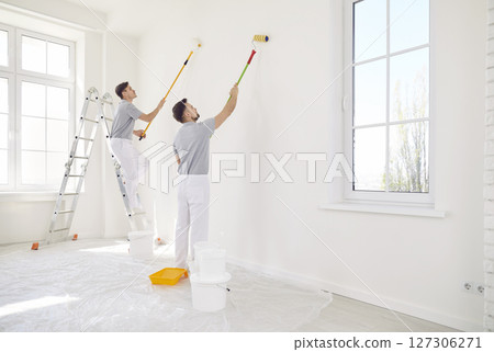 Male painters or construction workers painting walls in white color with paint roller brush 127306271