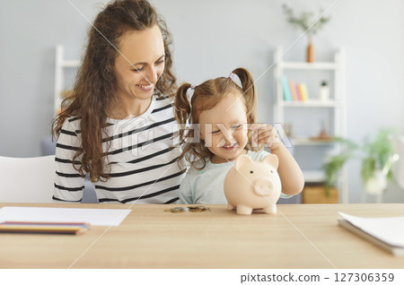 Mother And Child Saving Money In A Piggy Bank Together At Home 127306359