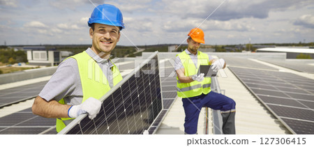 Team of electrical engineers installing photovoltaic solar panels and looking at camera. 127306415