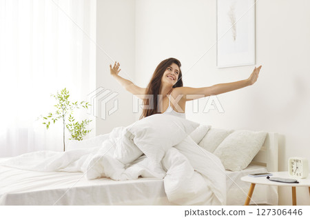 Relaxed brunette girl smiling and stretching after waking up in cozy bed, enjoying weekend morning. 127306446