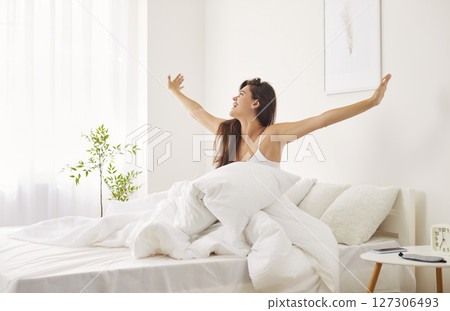 Happy Woman Waking Up And Stretching In Bed While Looking Out The Window Happy Woman Waking Up And Stretching In Bed While Looking Out The Window 127306493