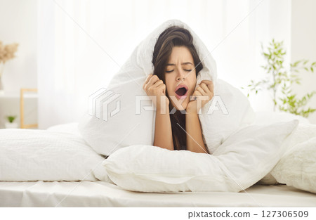 Young woman woke up lying in soft bed under soft blanket yawning, feels tired after night sleep, wants more 127306509