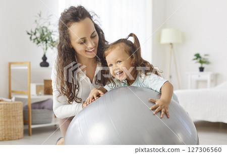 Happy mother and her little daughter playing with a yoga ball and having fun together Happy mother and her little daughter playing with a yoga ball and having fun together 127306560