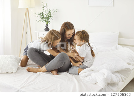 Happy mother and her children having fun, tickling little girl, playing together during weekend. Happy mother and her children having fun, tickling little girl, playing together during weekend. 127306563