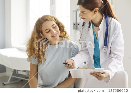 Friendly doctor talking with a woman patient standing in office in clinic. Friendly doctor talking with a woman patient standing in office in clinic. 127306620