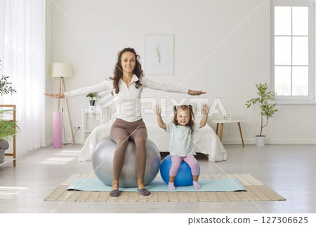 Mother sitting on fit ball with child daughter and doing sport exercises at home together Mother sitting on fit ball with child daughter and doing sport exercises at home together 127306625