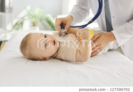 Toddler lying on clinic couch while friendly pediatrician listening to his heartbeat during checkup. 127306702