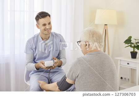 Caregiver smiling while measuring blood pressure of senior patient during routine checkup in clinic. 127306703