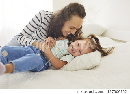 Loving young mother and her daughter sharing joyful moments in sunlit bedroom, playing and laughing. Loving young mother and her daughter sharing joyful moments in sunlit bedroom, playing and laughing. 127306732