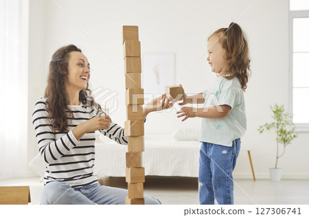 Young family with a child son playing an educational wooden pyramid game at home together. 127306741