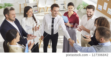 Team of professionals applauding and shaking hands with colleague, celebrating success together. Team of professionals applauding and shaking hands with colleague, celebrating success together. 127306842