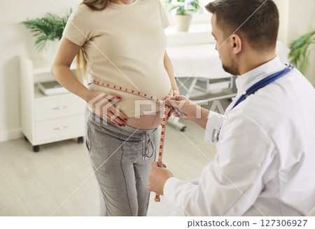 Doctor measuring belly of pregnant woman with tape measure, controlling prenatal weight Doctor measuring belly of pregnant woman with tape measure, controlling prenatal weight 127306927