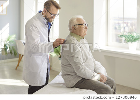 Professional doctor examining senior man patient, listening his breathing with stethoscope on back Professional doctor examining senior man patient, listening his breathing with stethoscope on back 127306946