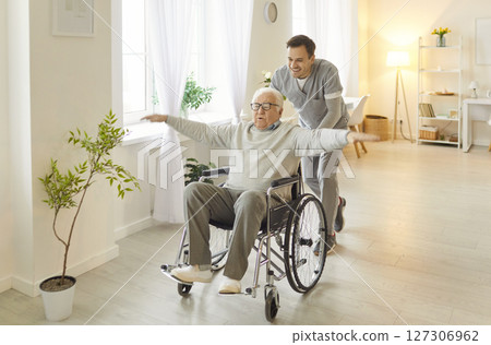 Male caregiver having fun together with his senior man patient, riding him in wheelchair Male caregiver having fun together with his senior man patient, riding him in wheelchair 127306962