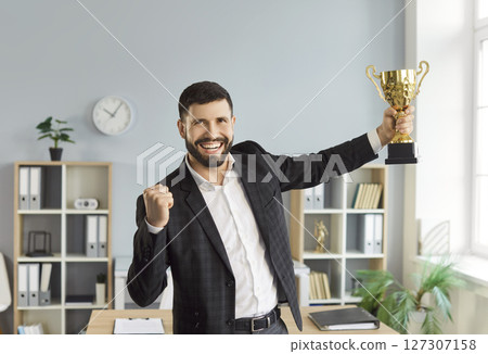 Happy man holding the trophy award for success in business standing in office 127307158