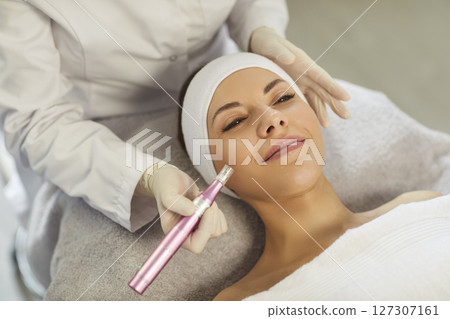 Cosmetologist, dermatologist beautician performing female face microneedling using dermapen  127307161
