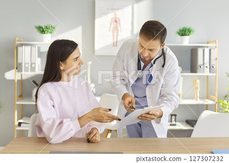 Doctor holding report file with appointment and prescribe treatment to female patient in clinic Doctor holding report file with appointment and prescribe treatment to female patient in clinic 127307232