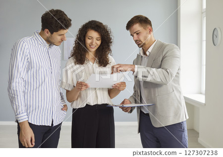Man realtor standing with young couple in new apartment discussing contract buying property Man realtor standing with young couple in new apartment discussing contract buying property 127307238