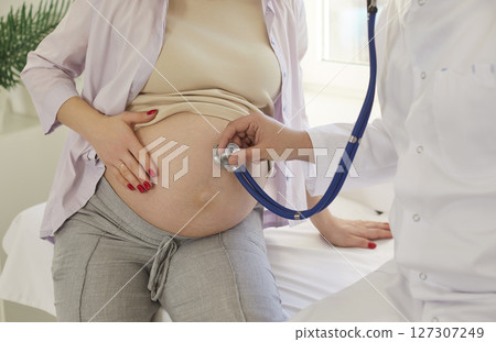 Gynecologist doctor examining heartbeat in abdomen of pregnant woman with stethoscope. 127307249