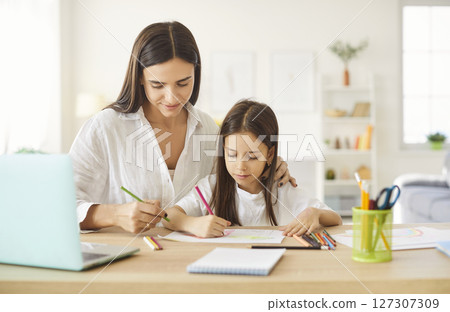Mother and daughter sitting at desk and drawing picture with colored pencils together Mother and daughter sitting at desk and drawing picture with colored pencils together 127307309