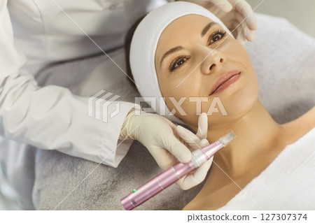 Woman receiving apparatus facial treatment procedure from cosmetologist in beauty wellness salon. Woman receiving apparatus facial treatment procedure from cosmetologist in beauty wellness salon. 127307374