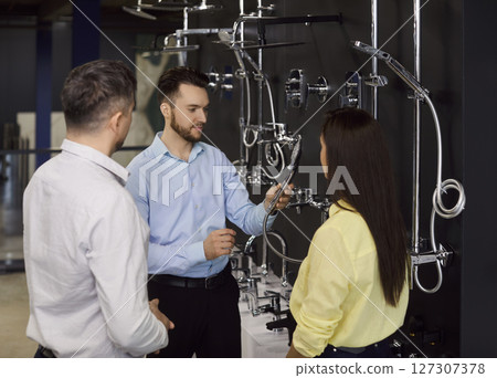 Man shop assistant recommending faucet or shower for family couple, posing in plumbing store Man shop assistant recommending faucet or shower for family couple, posing in plumbing store 127307378