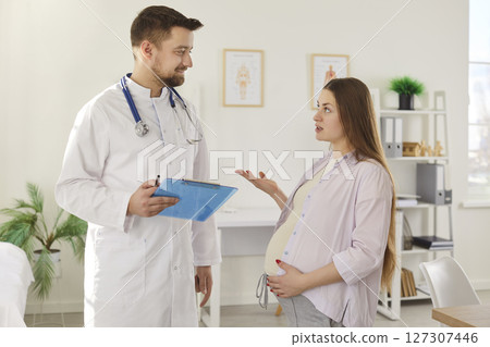 Young pregnant woman talking with her male gynecologist doctor in hospital or medical clinic. Young pregnant woman talking with her male gynecologist doctor in hospital or medical clinic. 127307446