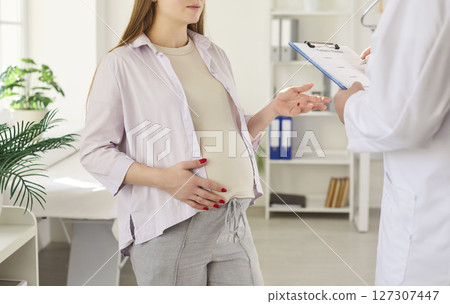 Doctor filling medical form of pregnant woman consulting expectant mom providing prenatal care Doctor filling medical form of pregnant woman consulting expectant mom providing prenatal care 127307447