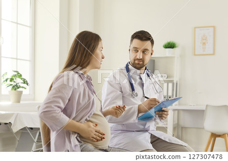 Male doctor sitting in medical office, listening to pregnant woman and discussing health concerns. 127307478