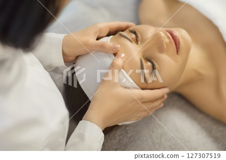 Young woman enjoying relaxing face massage during professional skincare spa treatment at spa salon. Young woman enjoying relaxing face massage during professional skincare spa treatment at spa salon. 127307519