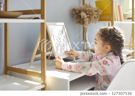 Little girl playing with puzzle on whiteboard, learning letters and numbers during education at home 127307536