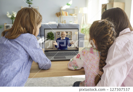 Family sitting at home and having online video call with grandfather using laptop. Family sitting at home and having online video call with grandfather using laptop. 127307537