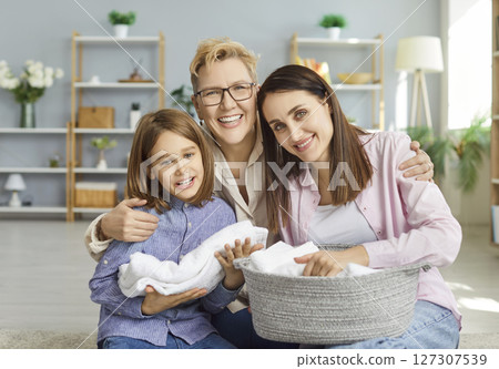 Granny, mother and small son posing together embracing and folding washed towels doing domestic work 127307539