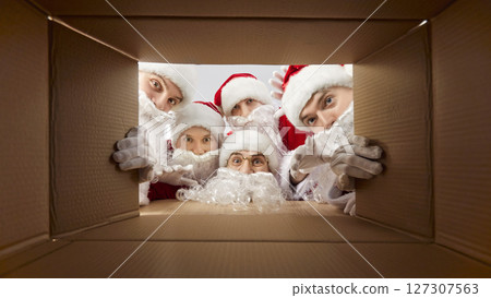 People in Santa Claus hats looking inside cardboard box preparing package delivery on xmas. People in Santa Claus hats looking inside cardboard box preparing package delivery on xmas. 127307563