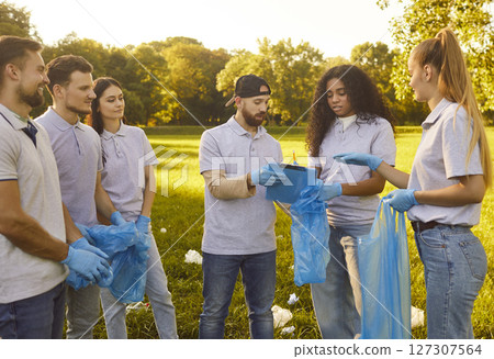 Young people volunteers holding trash bags working in summer park collecting garbage outdoors. Young people volunteers holding trash bags working in summer park collecting garbage outdoors. 127307564